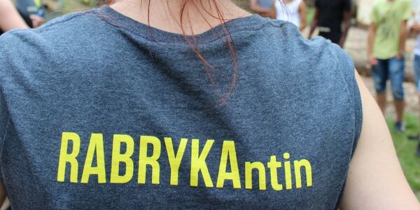 Rabrykant:in werden! Zu sehen ist eine Person, die mit dem Rücken zur Kamera steht. Auf ihrem grauen T-Shirt kann man den gelben Schriftzug Rabrykantin lesen.