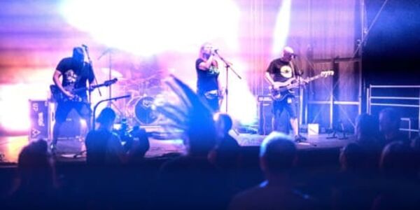 Eine Band mit drei Männern steht auf einer Bühne vor vielen Menschen.